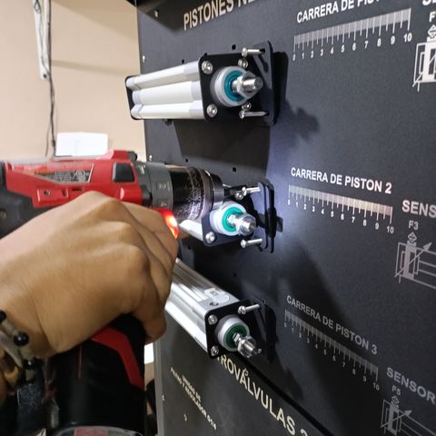 Técnico de SYSTRONIC ensamblando con taladro un cilindro neumático durante la fabricación de un banco didáctico de automatización industrial