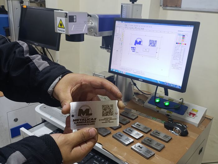 Técnico de SYSTRONIC verificando una placa metálica grabada con láser, junto al software de diseño y la máquina de grabado